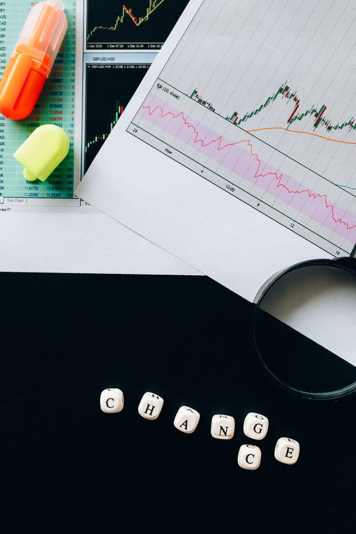 Home A flat lay image featuring financial charts, highlighters, and dice spelling 'CHANGE' on a black background.