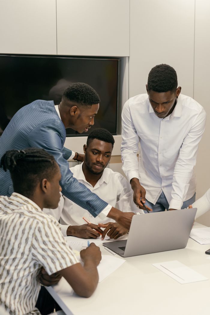 why-choose-us Four men collaborate on a project using a laptop in a modern office environment.